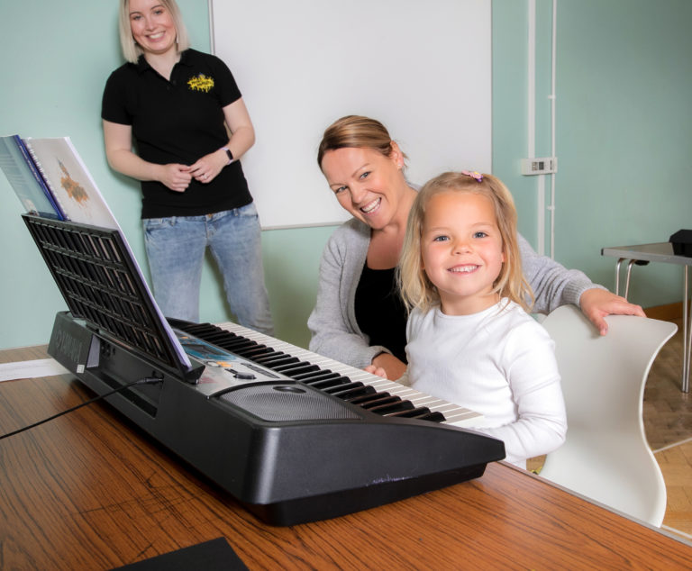 Child looking happy at a piano lesson with mum and teacher