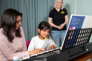 Piano class taking place, teacher watching over attentively.